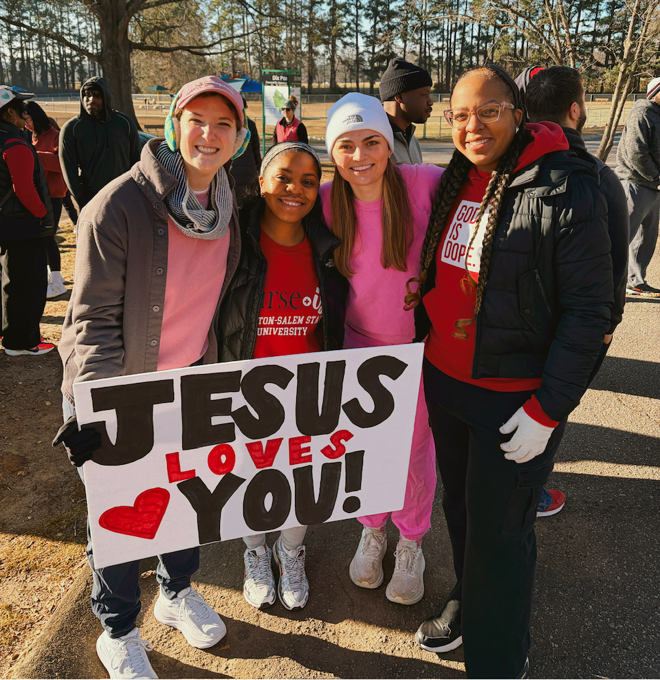 Group of people outdoors holding a sign that reads 'Jesus Loves You'.